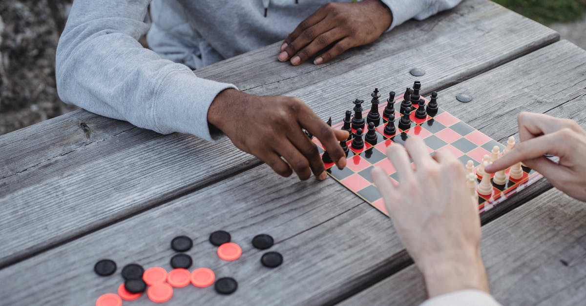 How does someone end a game and win with less points and when their opponent still has tiles - From above of crop unrecognizable multiethnic male friends sitting at wooden table in park and playing chess