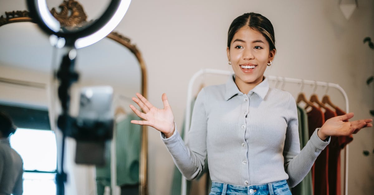 How does the Digi-Clone choose what gun to use? - Happy young ethnic female blogger in blouse and jeans standing in wardrobe and using phone with ring light while filming vlog about trendy clothes near mirror