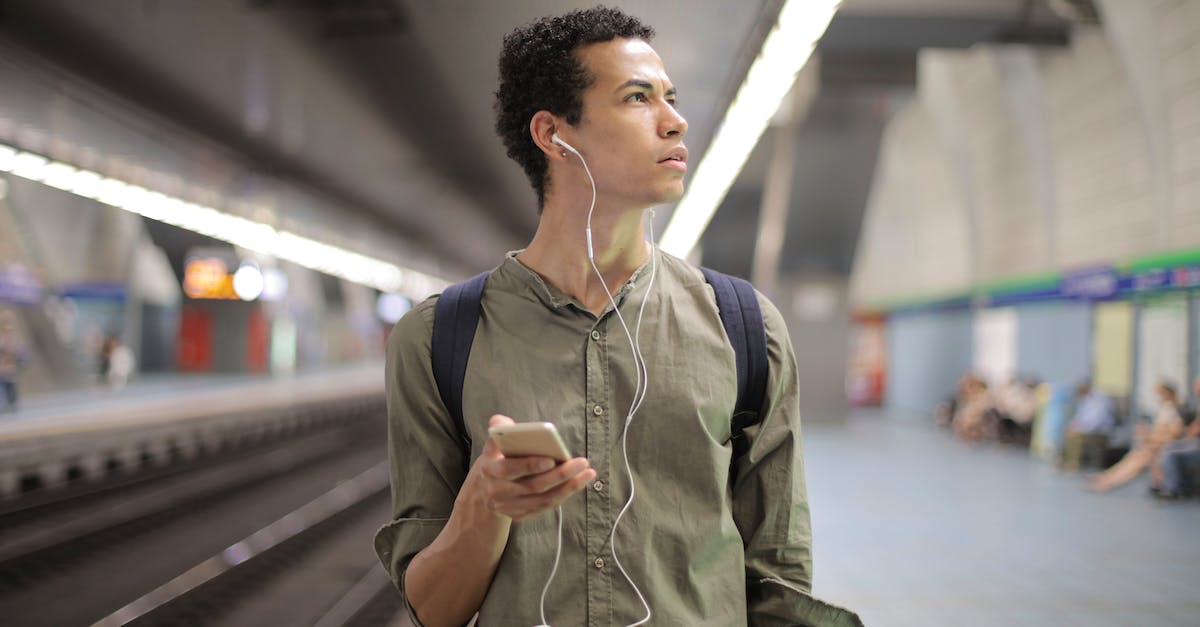 How does Ubsoft's app "ctOS mobile", work from the main Watch_Dogs player's perspective? - Young ethnic man in earbuds listening to music while waiting for transport at contemporary subway station