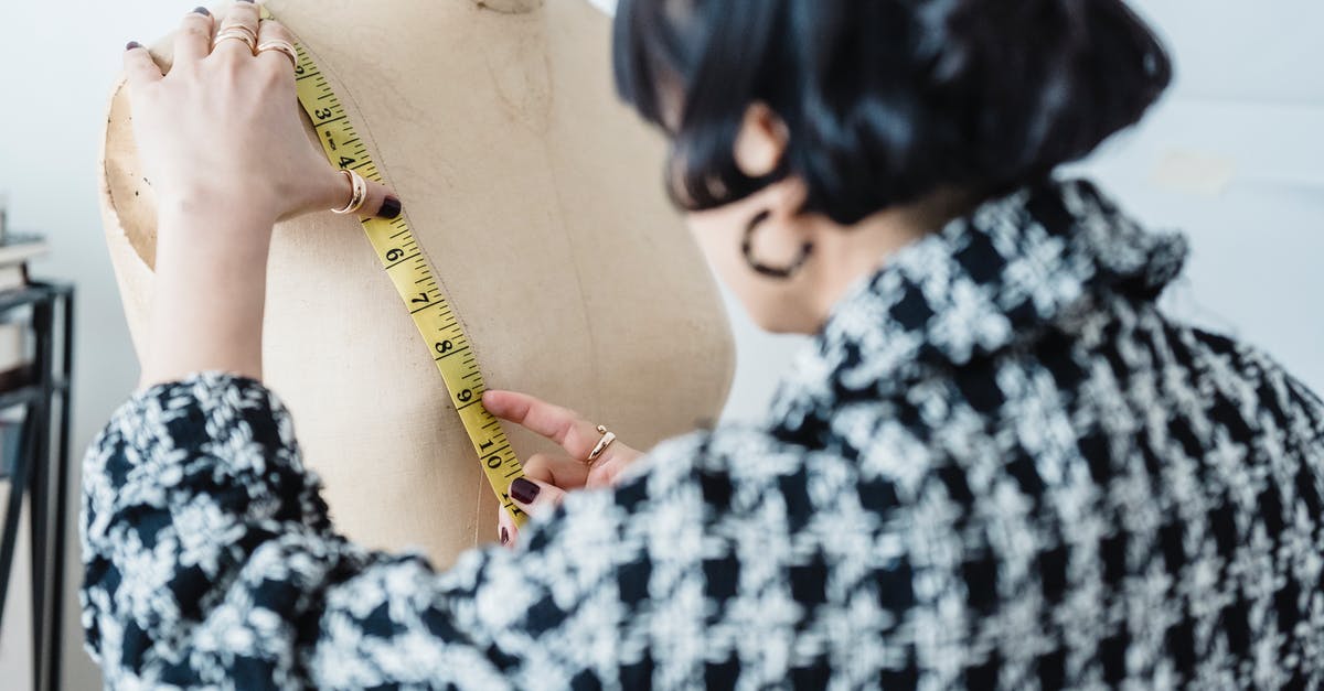 How does Zac's size changes work? - Back view of crop anonymous female tailor in checkered wear with flexible ruler measuring chest of dummy in workshop
