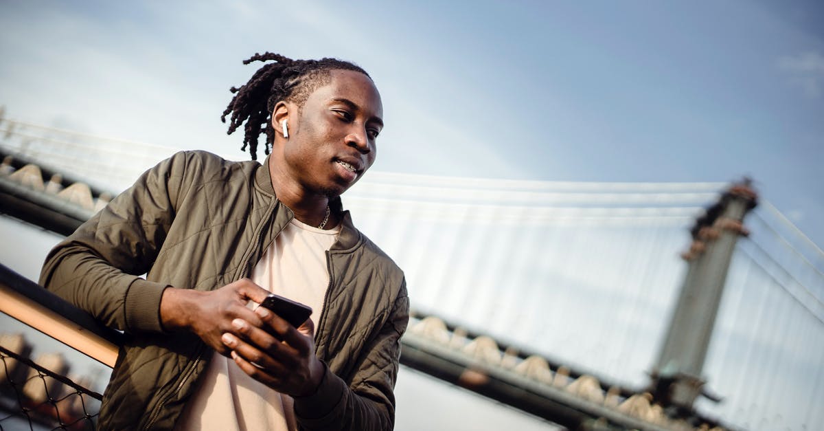 How far away do I need to be away from guards and sound bugs to avoid being heard? - From below of smiling African American guy in wireless earphones using cellphone while standing on embankment alone How far away do I need to be away from guards and sound bugs to avoid being heard? - From below of smiling African American guy in wireless earphones using cellphone while standing on embankment alone
