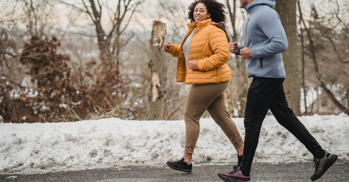 How is road completion determined? - Full body of positive curvy African American woman and black coach looking at each other while jogging on asphalt walkway in winter time