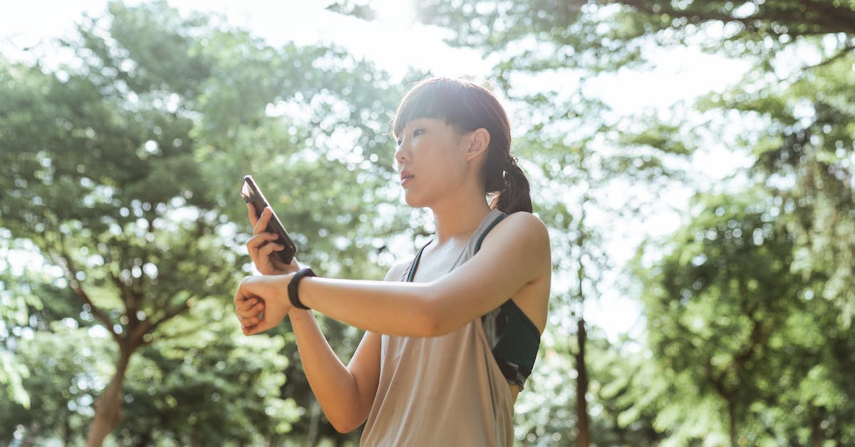 How is the park rating calculated? - Low angle side view of fit Asian female athlete in wearable device and activewear surfing internet on cellphone during workout in park in sunlight in back lit