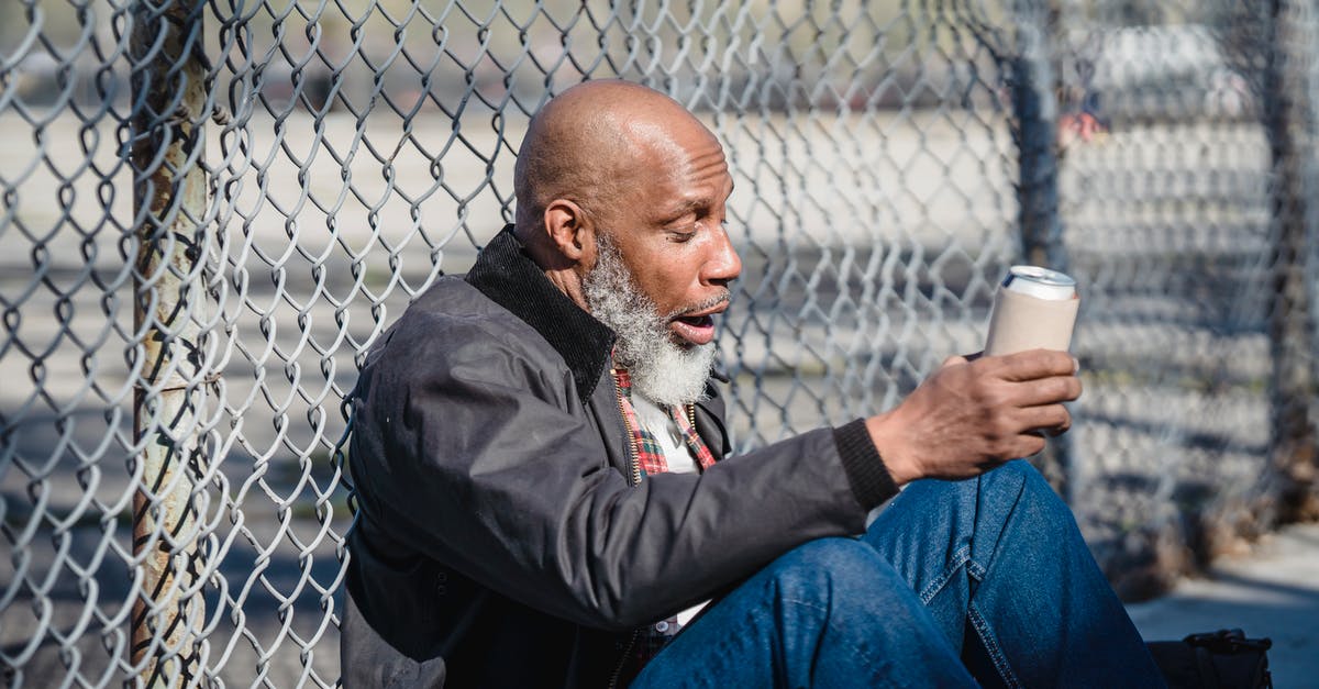How long can a wire go? - Side view of black homeless bald man sitting on street with beer can in hand and leaning on wire railing