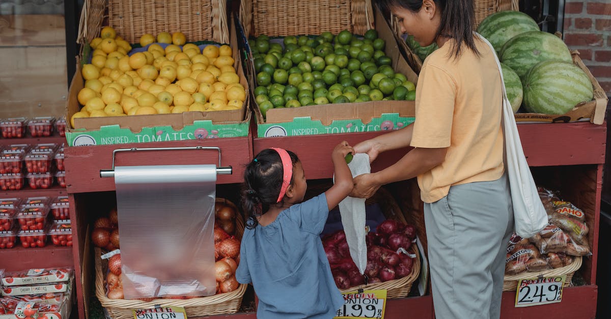How many children can I adopt? - Back view of Asian girl picking ripe limes from box to eco friendly bag while shopping with mother in market