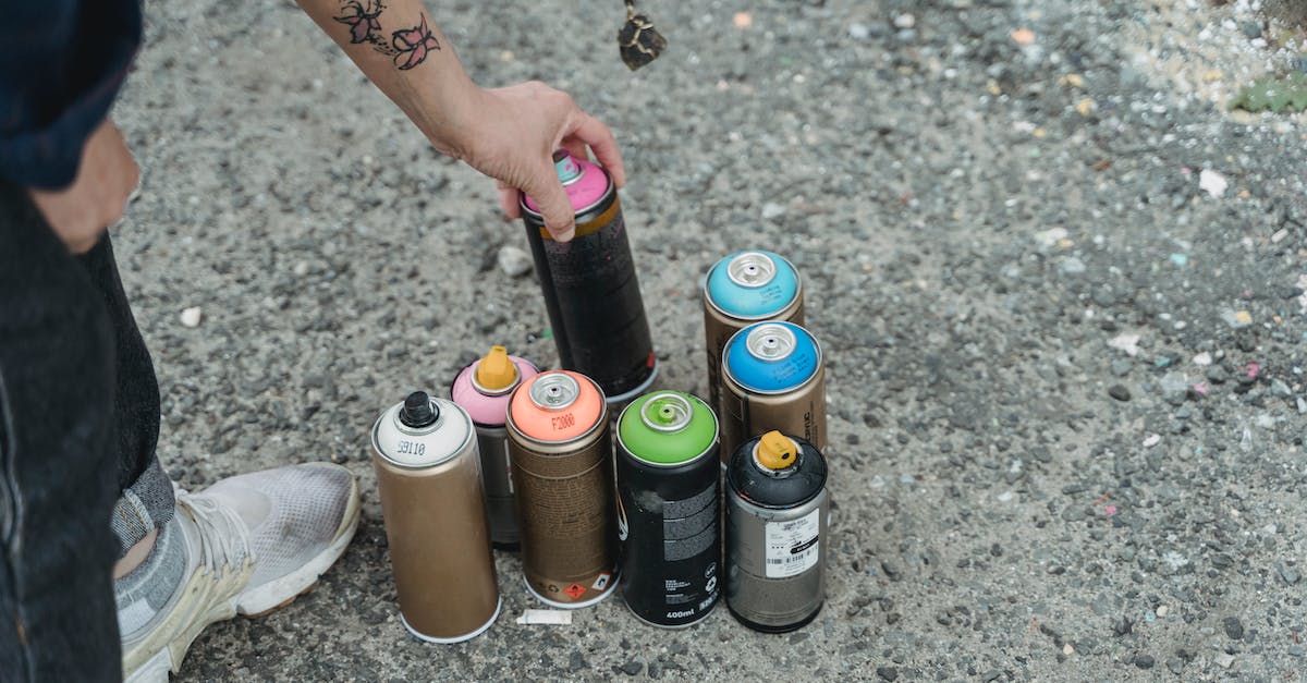How many first gen PS3s are affacted by and how can I avoid YLOD? - Crop anonymous person in sneakers with tattoo and heap of multicolored spray paint cans on ground standing on street in city