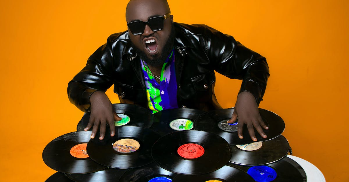How many players must own Mario Bros for 2 player mode? - Skilled African American male DJ in leather jacket standing in studio while scratching abundance of various vinyl records on orange background