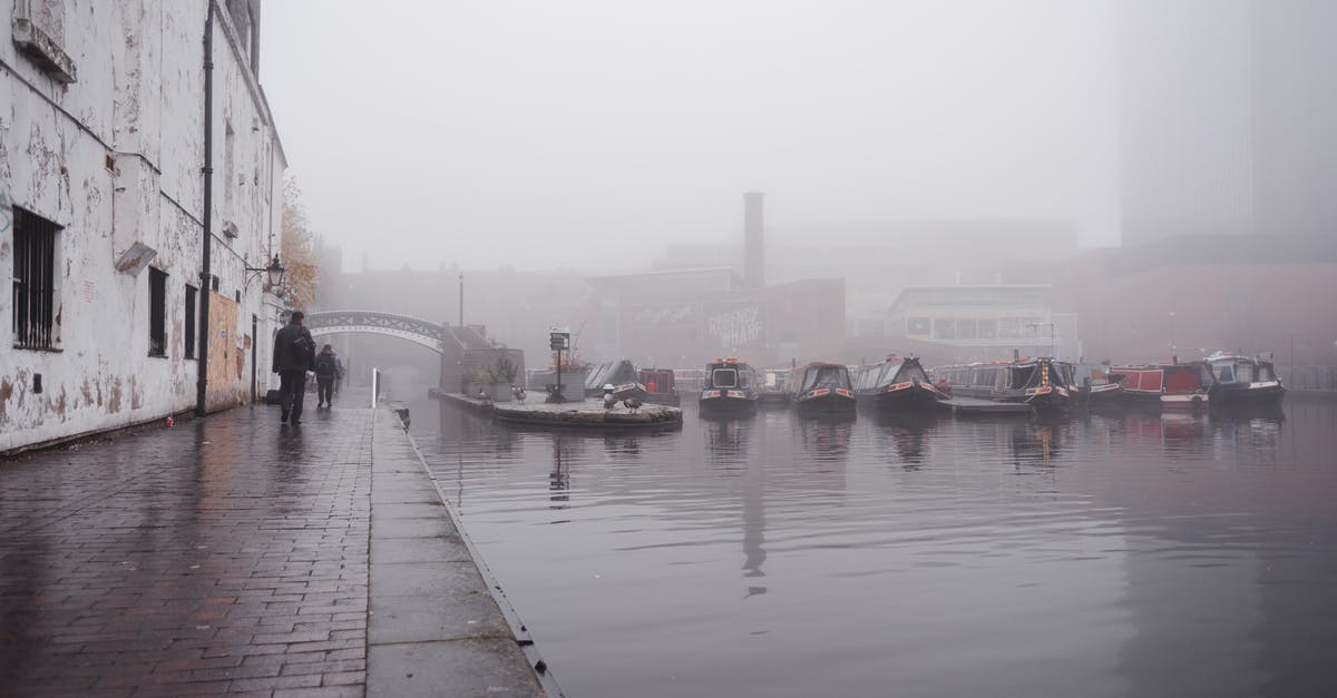 How many players to fill a channel - Many boats moored on calm water surface near paved waterfront with people walking near shabby building in town on foggy weather