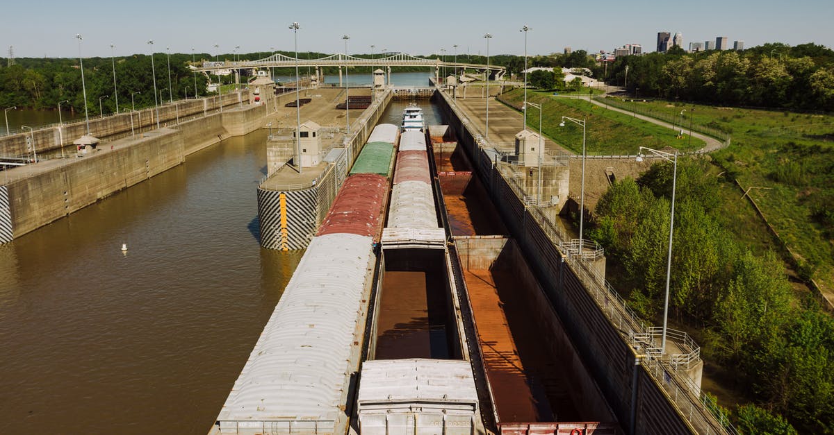 How many players to fill a channel - From above of old barge carrying heavy metal containers on canal between growing trees in city port under sky