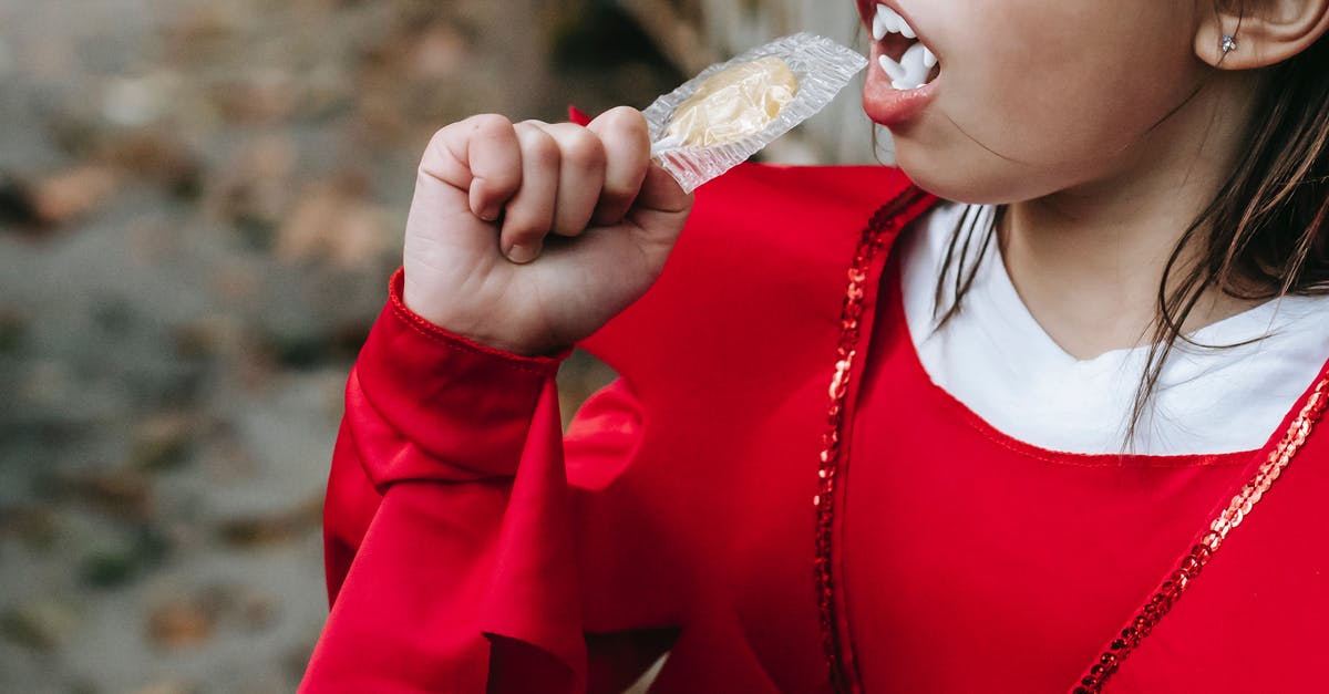 How much candy for walking Pokemon? - Crop unrecognizable kid in red devil costume with fangs on Halloween eating lollipop in autumn day in street How much candy for walking Pokemon? - Crop unrecognizable kid in red devil costume with fangs on Halloween eating lollipop in autumn day in street