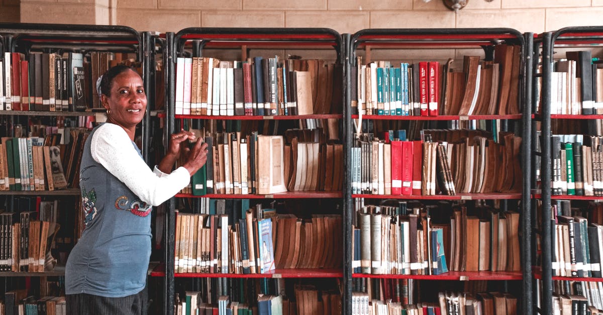 How much storage does Nier take on ps3? - Side view of content mature Hindu female picking textbook from bookcase with assorted literature while looking at camera in library