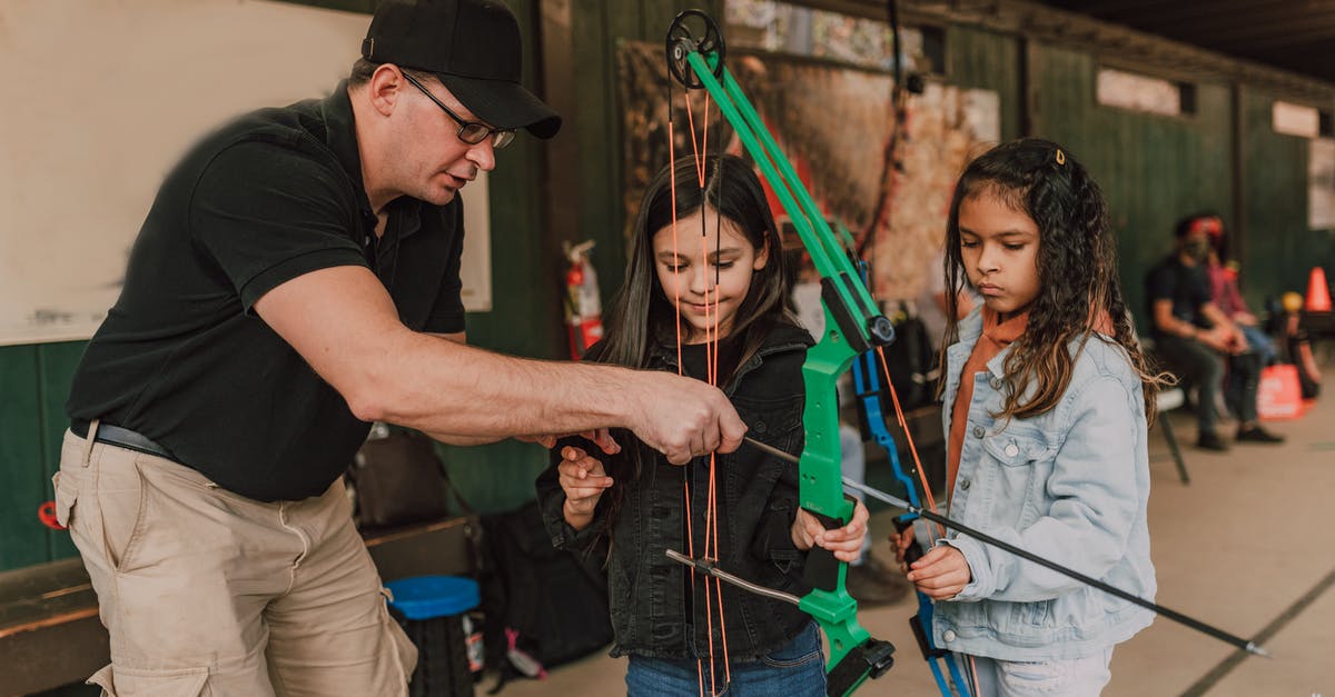 How to aim at long range with 2x scopes? - Adult male archery coach teaching adorable little multiethnic girls to shoot with bow and arrow during classes in range