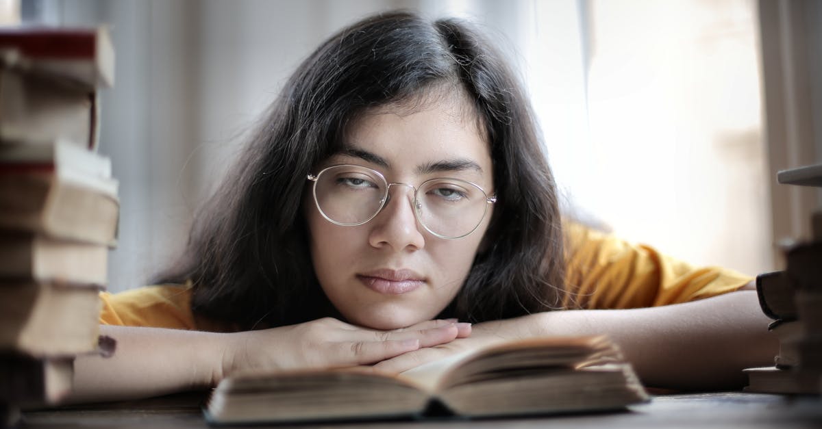How to assign people to tasks? - Exhausted ethnic female student in eyeglasses lying on table with stacks of textbooks while working on assignment and looking at camera