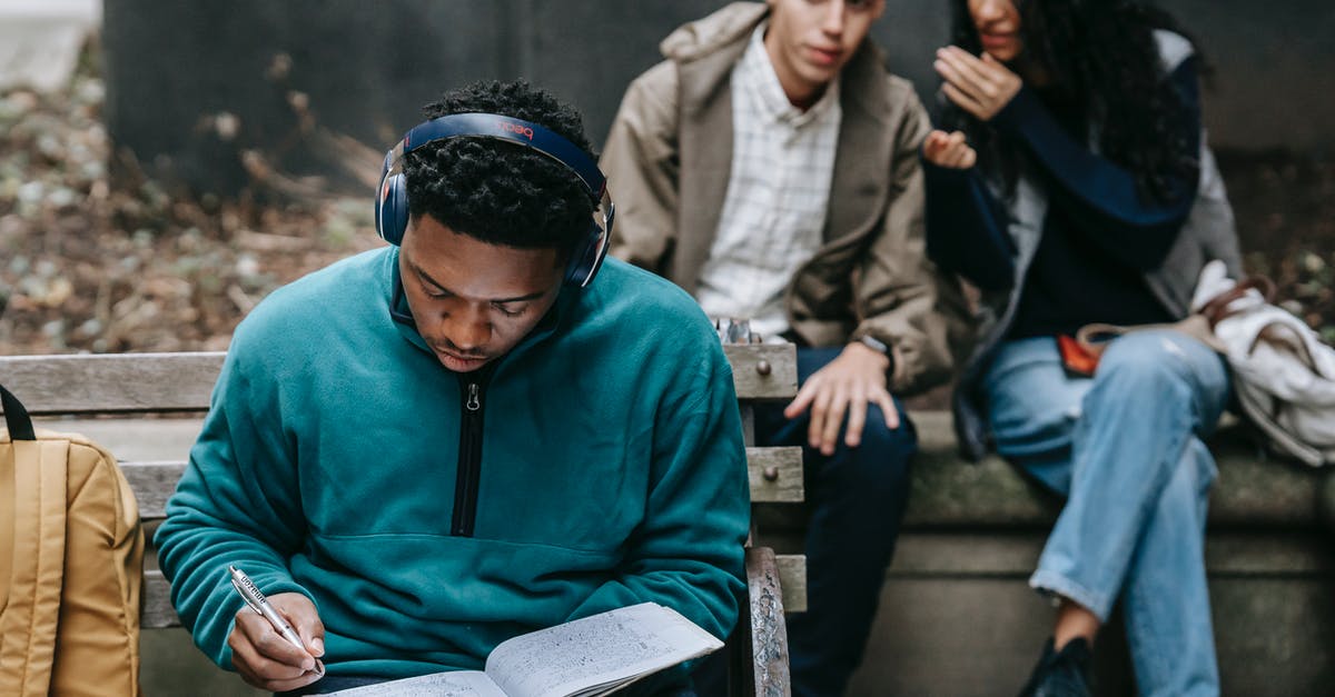 How to assign people to tasks? - Crop young ethnic man and woman sitting on bench and gossiping about concentrated African American male student listening to music in headphone and doing homework assignment