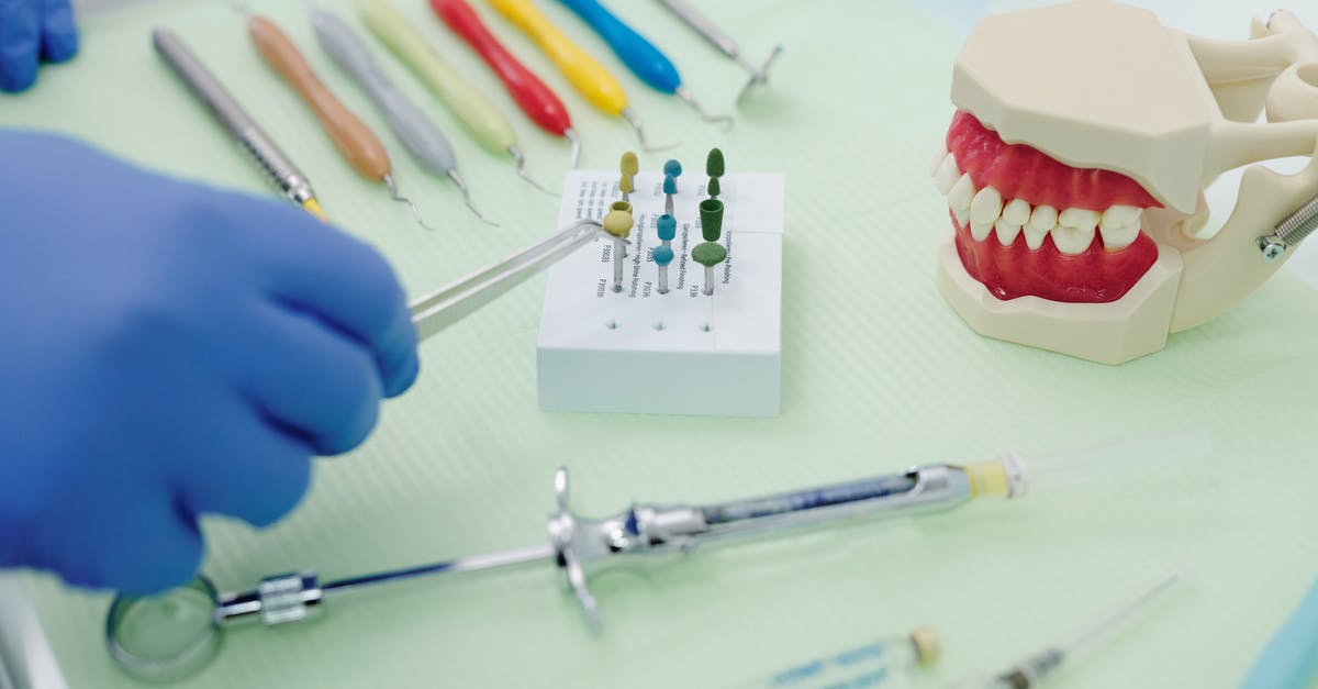 How to cast curse as aura? - From above of crop faceless orthodontist in latex gloves and tweezers working at medical table with cast jaw and set of syringes near periodontal scalers
