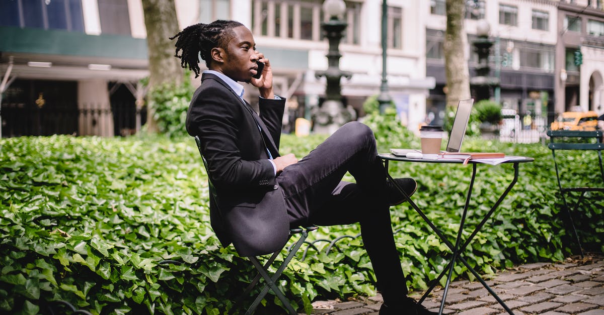How to chat to all - Side view serious African American businessman in black formal wear sitting at table in city park with legs crossed and having conversation via modern smartphone How to chat to all - Side view serious African American businessman in black formal wear sitting at table in city park with legs crossed and having conversation via modern smartphone