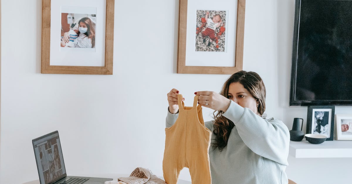 How to choose save device for downloads on Xbox Live - Happy young mother with long hair in casual sweatshirt folding clothes of baby while sitting at table with laptop in modern light apartment