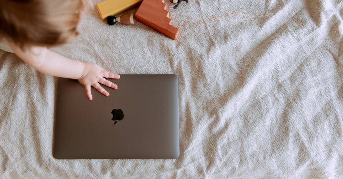 How to circumvent game breaking bug in GTA: San Andreas (PC) - From above of crop faceless child sitting on bed with scattered multicolored details of wooden constructor and touching closed laptop with hand
