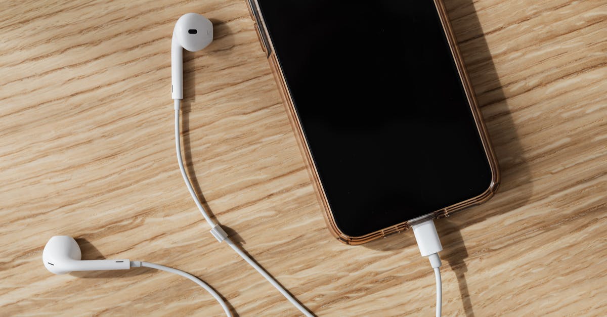 How to connect the audio to a separate speaker? - From above composition of white wired earphones and modern mobile phone with blank screen and connected charging cable placed on wooden surface in daylight How to connect the audio to a separate speaker? - From above composition of white wired earphones and modern mobile phone with blank screen and connected charging cable placed on wooden surface in daylight