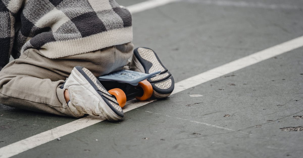 How to disable play time tracking? - Back view of anonymous little child wearing checkered sweater and sneakers sitting on penny board on sports ground on blurred background