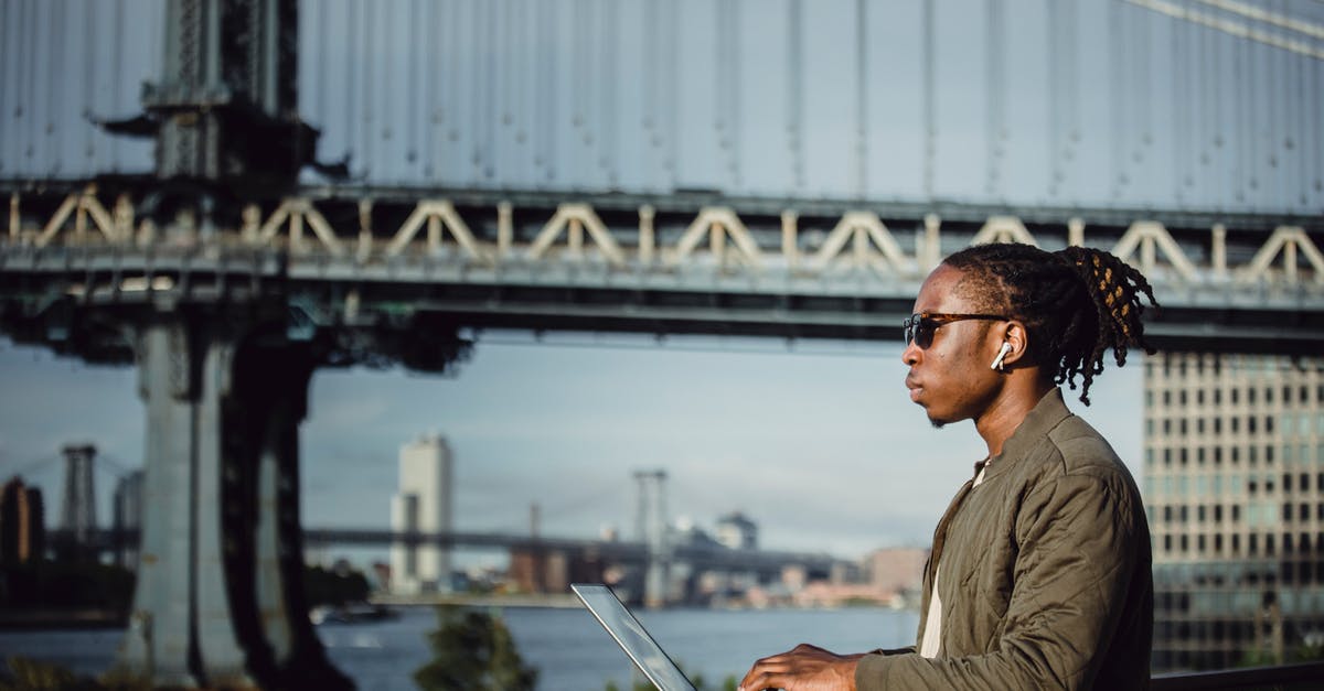 How to effectively keep a laptop cool while running a server? [closed] - Side view of young African American male in sunglasses with dreadlocks and wireless earphones working on laptop placed on terrace railing against blurred Manhattan Bridge