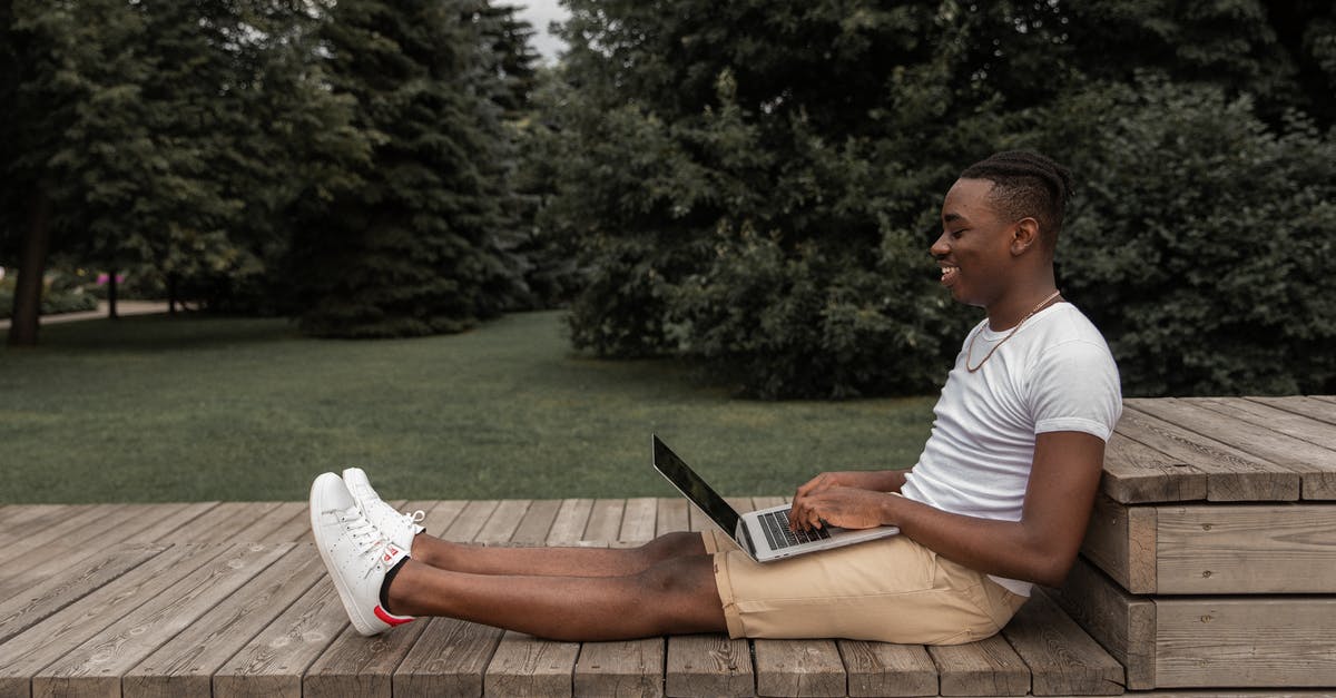 How to effectively keep a laptop cool while running a server? [closed] - Side view of African American male in casual outfit sitting on wooden surface and browsing netbook while looking at screen