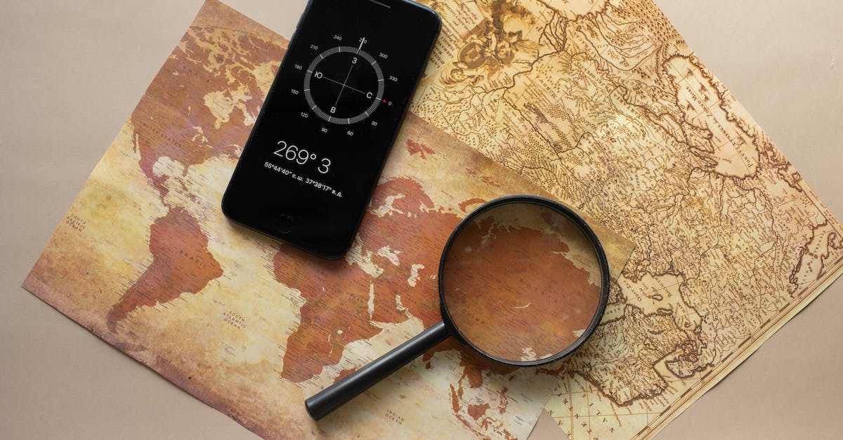 How to find villages? - Top view of magnifying glass and cellphone with compass with coordinates placed on paper maps on beige background in light room