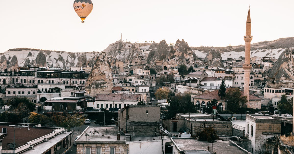 How to fly to an exact location with dragons? - Colorful air balloon flying above shabby buildings and tall tower in famous national park Goreme in Turkey against cloudless sky