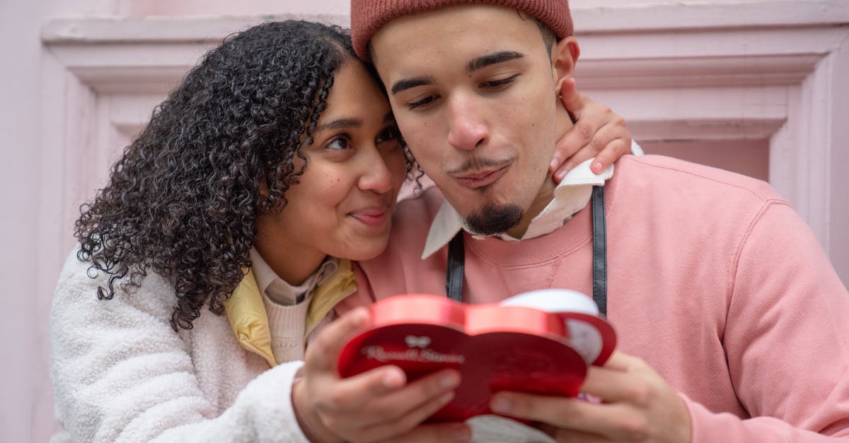 How to get cyber items in candy box 2? - Joyful young ethnic couple embracing and eating yummy candies from heart shaped gift box during anniversary celebration