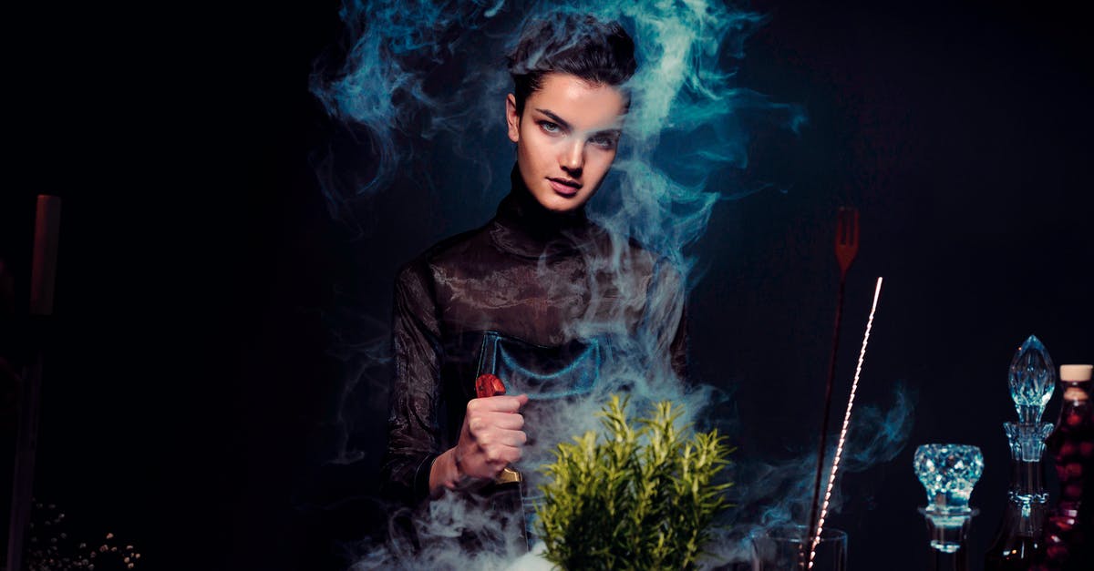 How to increment potion effects? - Graceful young female alchemist with knife in hand in black outfit preparing potion from various herbs among smoke in dark room