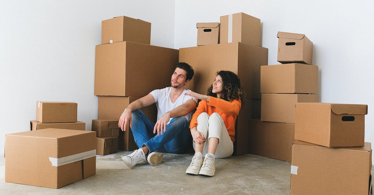 How to insert emoticons in the chat box? - Full body of young happy couple in casual clothes sitting on floor leaning on stack of cardboard boxes and chatting after relocation in new flat