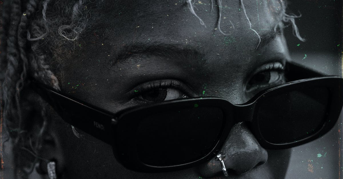 How to lower infamy? - Black and white crop attractive African American female with African hairstyle and nose piercing wearing trendy sunglasses on blurred street and looking at camera attentively