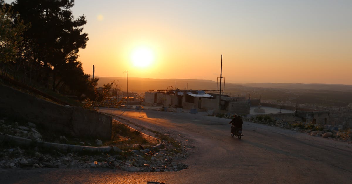 How to make totally self-sufficient Fallout 4 settlements without fast travel - Silhouettes of distant unrecognizable person riding motorbike on empty road in countryside near houses in settlement at sundown time on street
