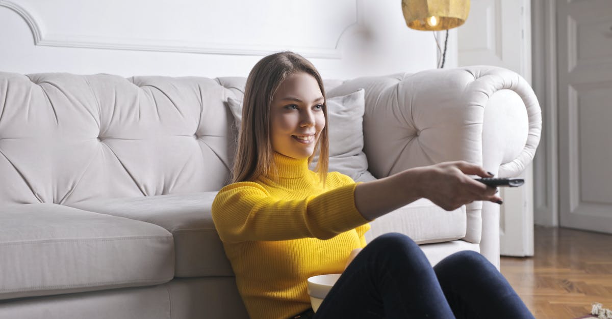 How to obtain as best as possible video quality in PSX/PS2 on modern TV - Joyful millennial female in casual clothes with bowl of snack using remote controller while sitting on floor leaning on sofa and watching movie in cozy light living room with luxury interior