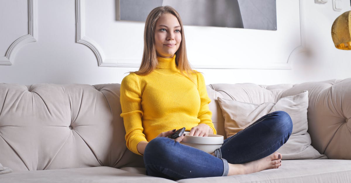 How to obtain as best as possible video quality in PSX/PS2 on modern TV - Positive young female in casual clothes sitting on cozy sofa with bowl of snacks and watching interesting film while spending time at home
