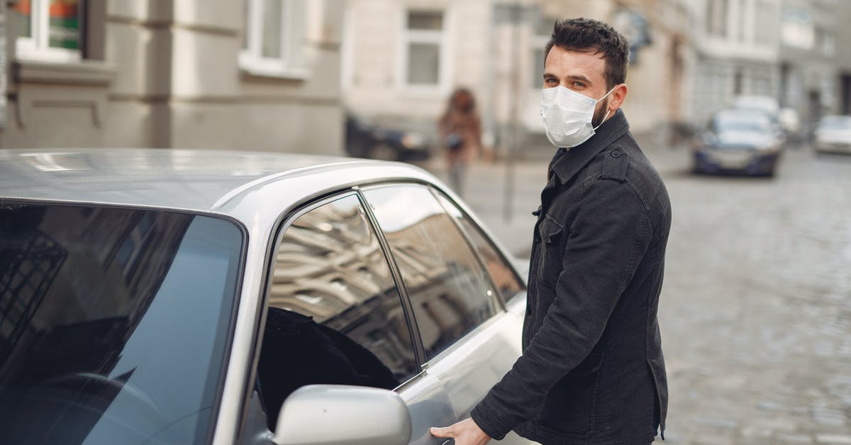How to open the world map? - Bearded male driver wearing warm jacket and protective facial mask opening door of auto on blurred city background during Coronavirus pandemic and looking at camera