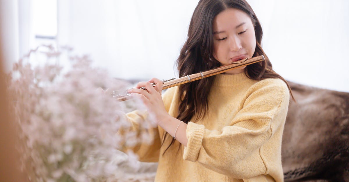 How to perform a flat spin? - Focused Asian female musician playing melody on flute while sitting in light room with blooming flowers at home during rehearsal