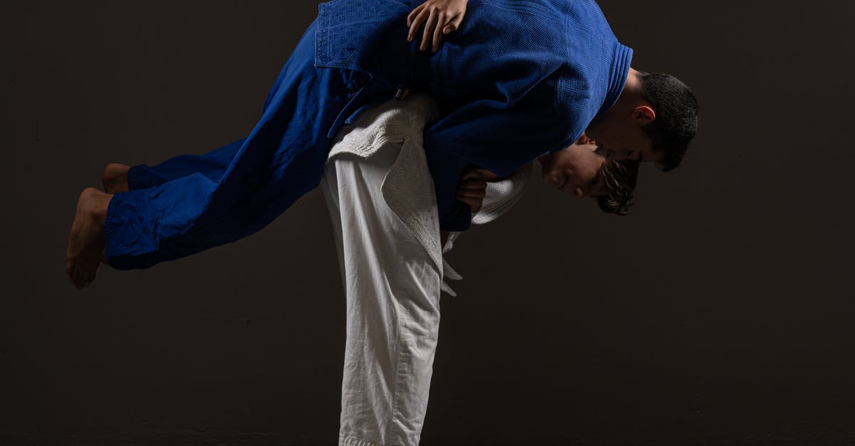 How to perform torture attacks? - Side view of young barefooted Asian male judokas in uniform fighting on floor against black background