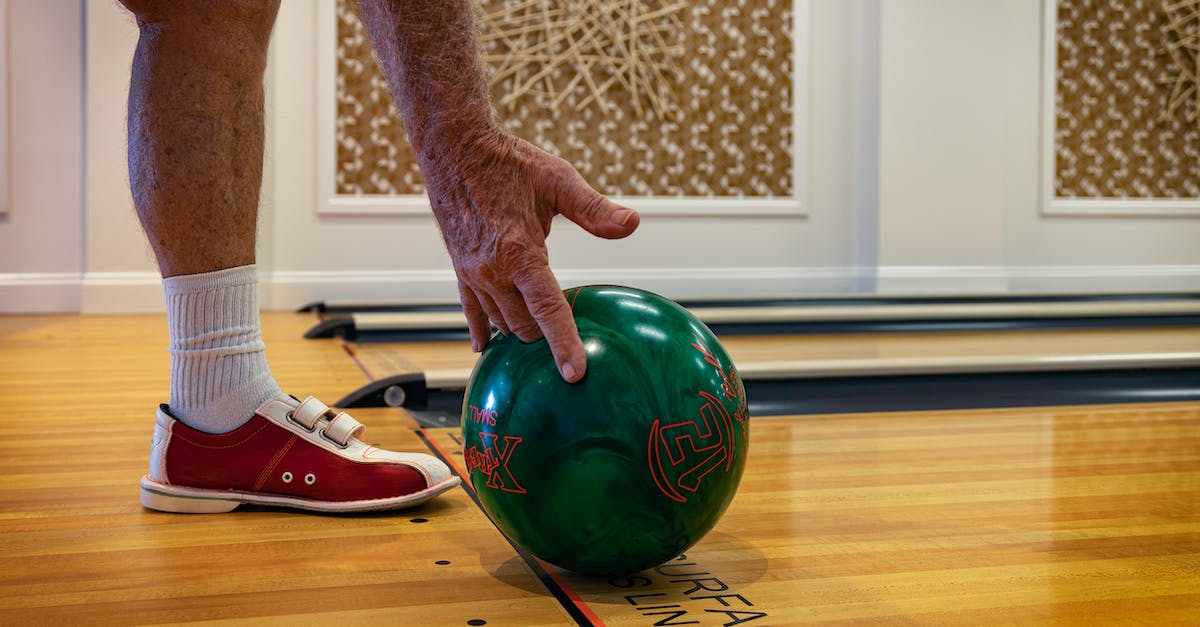 How to play a lane against tristana? - Crop anonymous sportsman in bowling shoes and socks rolling ball while playing bowling on wooden lane in modern bowling hall