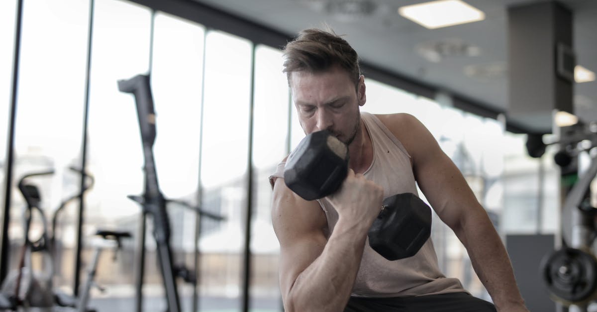 How to power a 200 z level pump stack - Low angle of powerful male athlete in sportswear performing exercise with heavy metal dumbbell while sitting on bench during workout in modern gym