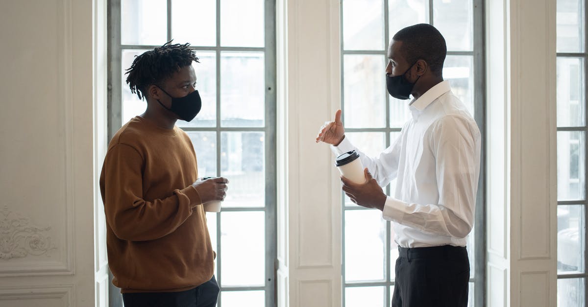 how to prevent wyverns from interrupting your boss battles - Side view of African American male executive in fabric mask with disposable hot beverage speaking with coworker while looking at each other indoors
