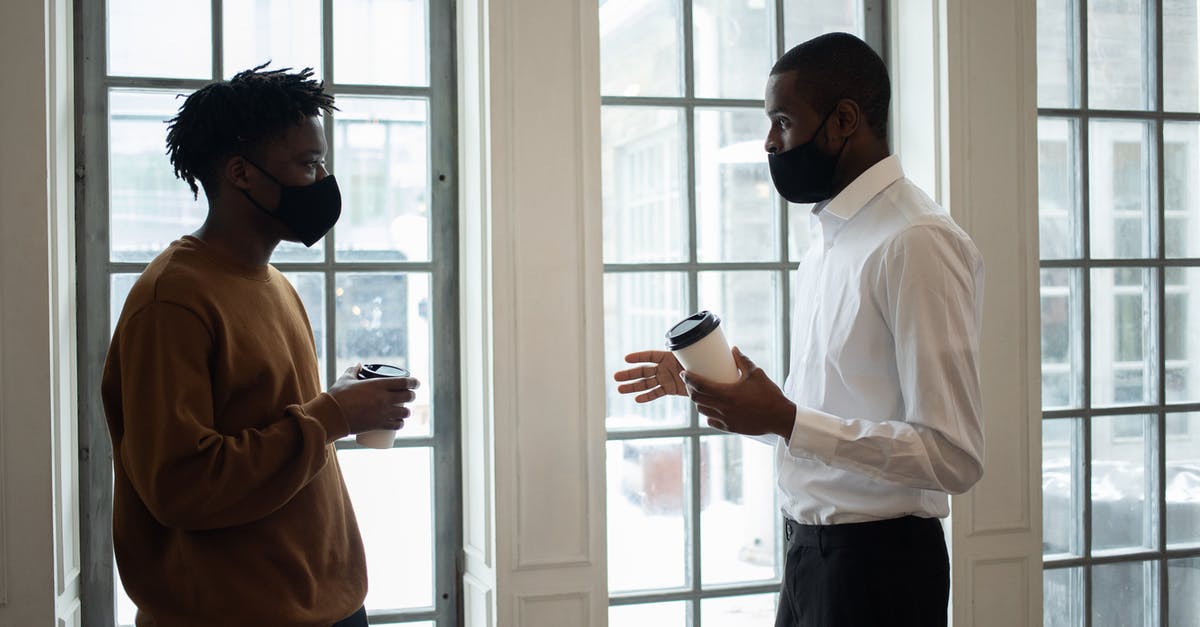 how to prevent wyverns from interrupting your boss battles - Side view of ethnic male director in fabric mask with coffee to go talking to employee while looking at each other indoors