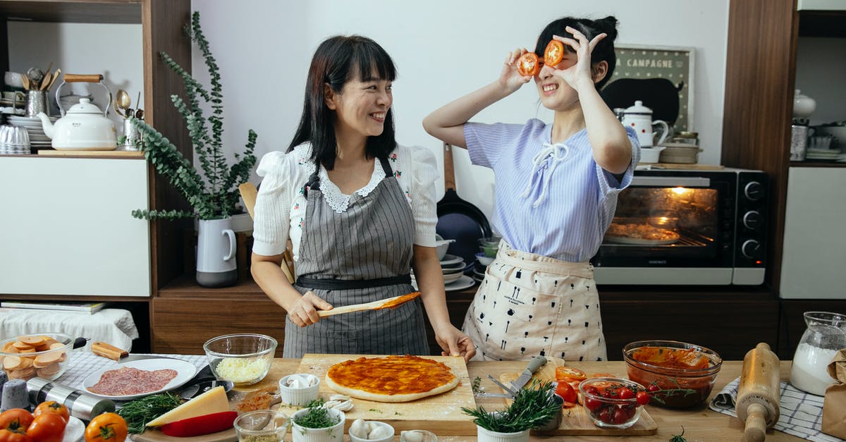How to put add-ons on Minecraft for Nintendo Switch? - Smiling Asian woman spreading tomato sauce on pizza dough while looking at funny female covering eyes with tomato slices in kitchen