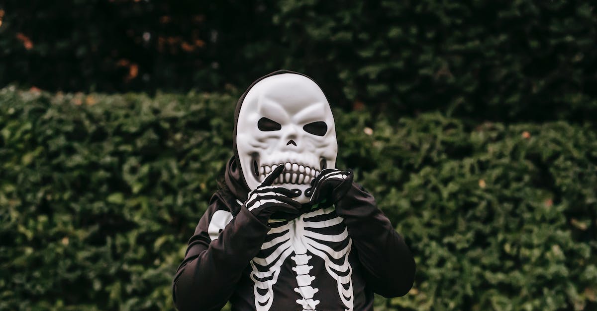 How to put zombie dwarf in a cage? - Unrecognizable child in skeleton costume for Halloween celebrating standing with hand near face in autumn street and looking at camera