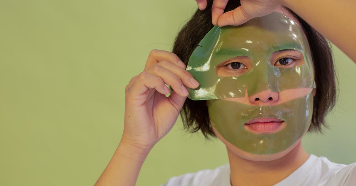 How to remove Rafflesia off an island - Young unemotional Asian male in white shirt removing cleansing mask sheet from face and looking at camera against green background