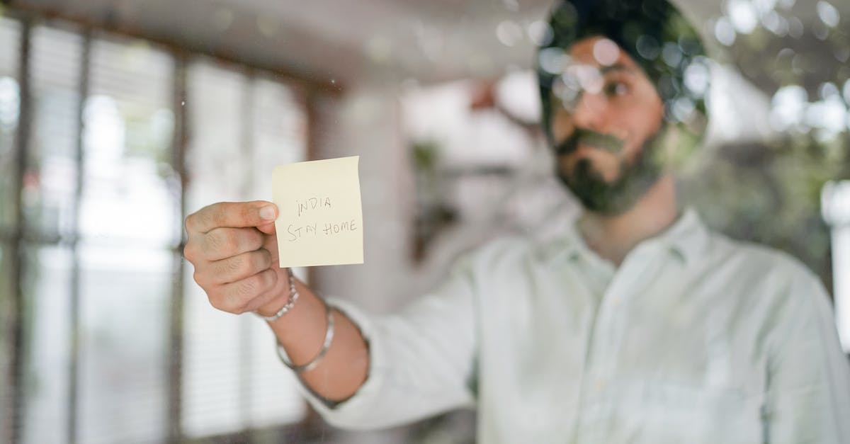 How to see difference between national and world wonders - Indian guy in turban and shirt with curled mustache sticking paper with INDIA STAY HOME inscription while standing behind glass wall during COVID 19 pandemic