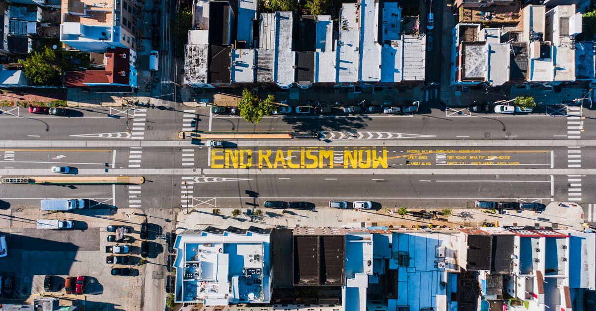 How to see what the builders are building right now? - Overhead view of asphalt roadway with vehicles between building roofs and colorful title about racism How to see what the builders are building right now? - Overhead view of asphalt roadway with vehicles between building roofs and colorful title about racism