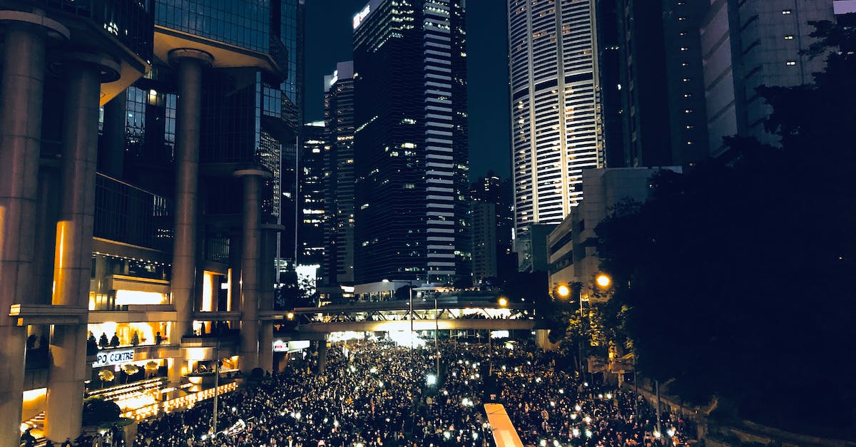 How to stop people from settling in our area? - From above of crowd of people standing on street in dark modern city centre during mass protest