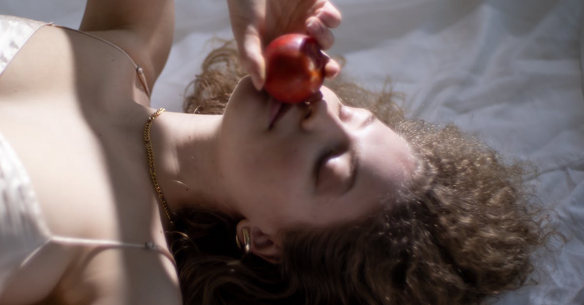 How to tell high-quality food from the rest in a stockpile? - From above of young female with eyes closed smelling ripe red apple while lying on white fabric