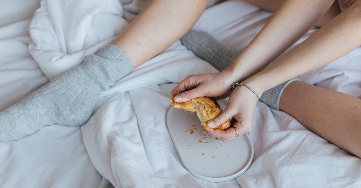 How to tell high-quality food from the rest in a stockpile? - Unrecognizable woman eating croissant on comfy bed at home